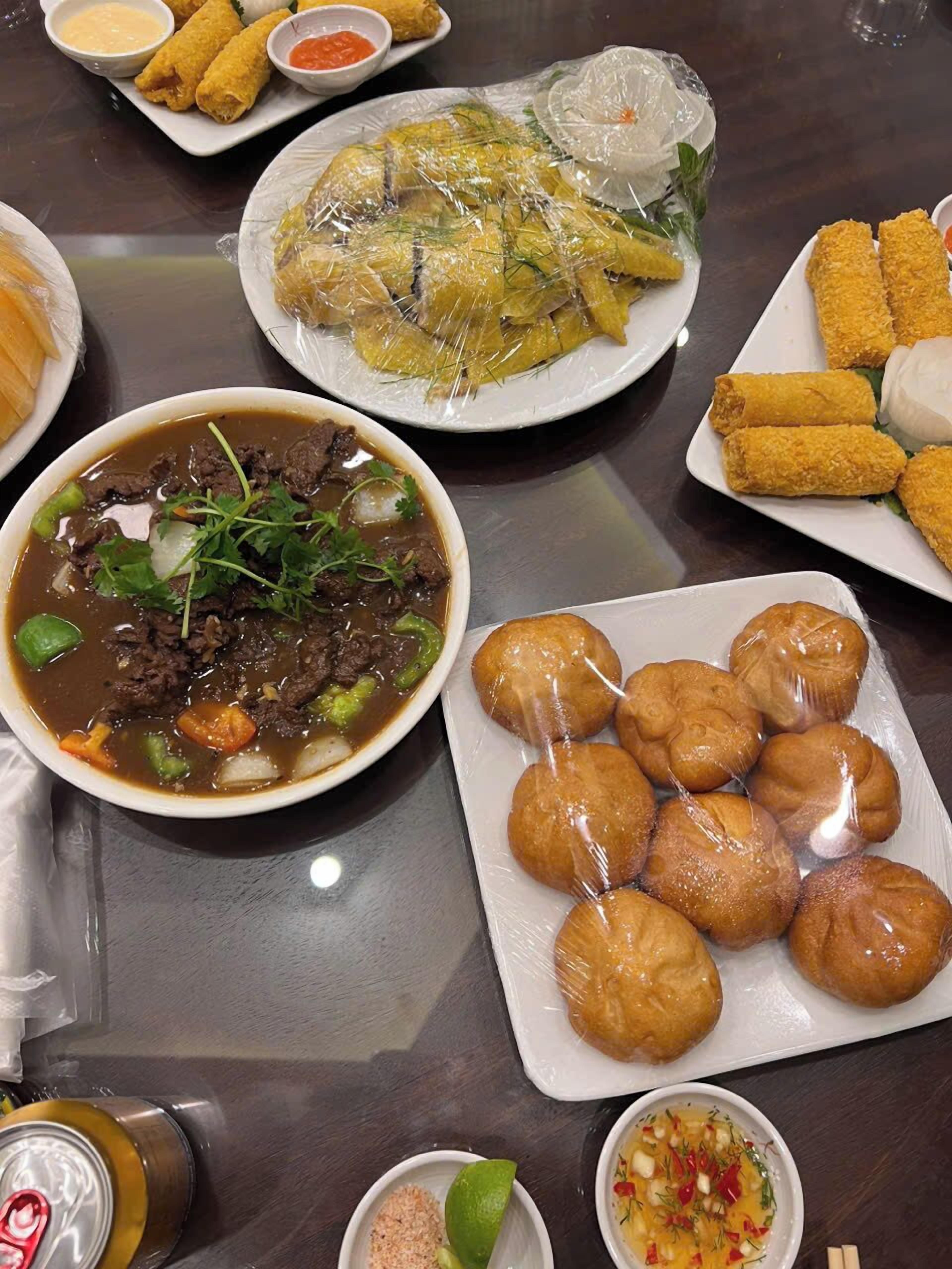 A table with various dishes including a bowl of beef stew, fried spring rolls, and other Asian cuisine.