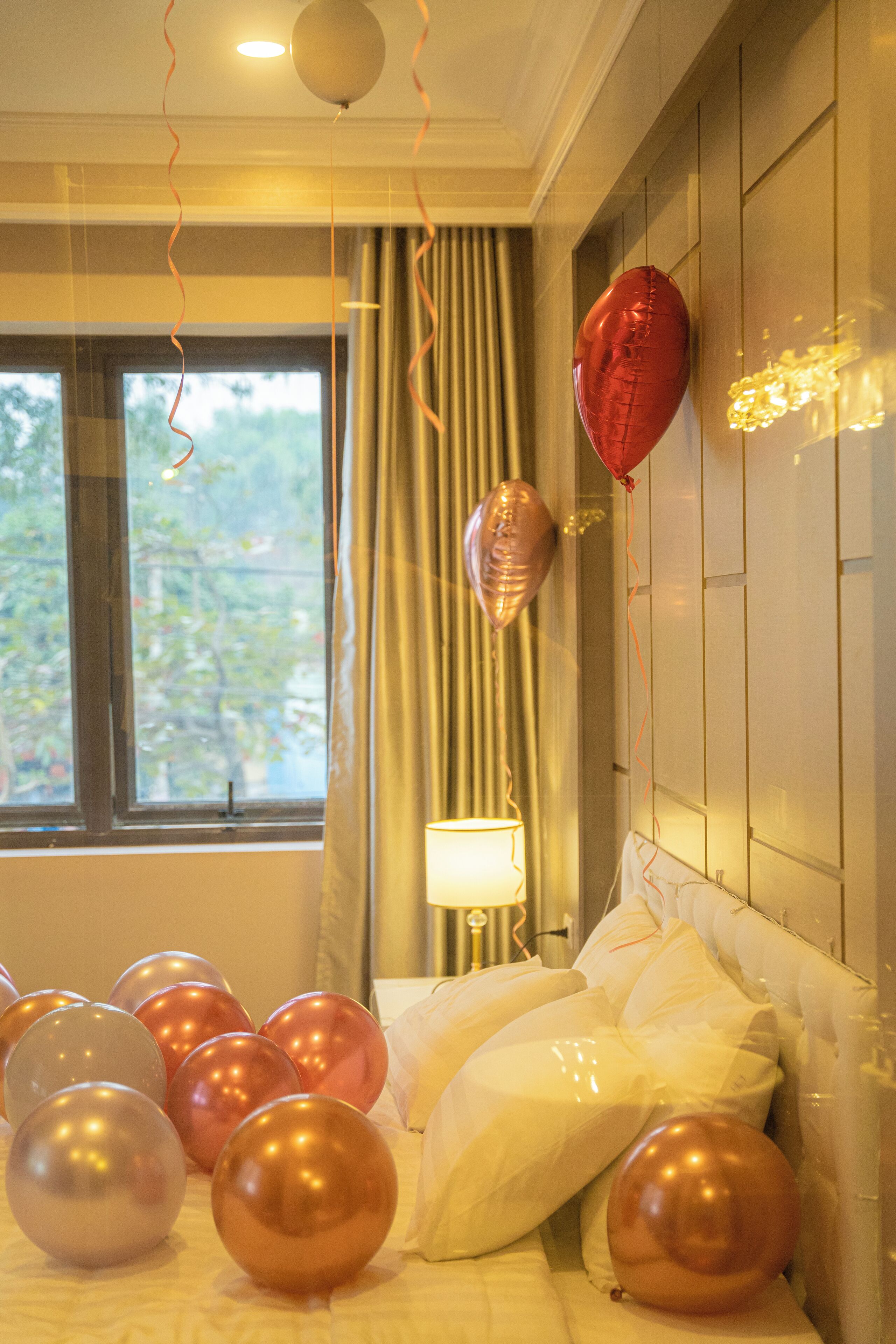 Une chambre d’hôtel avec un lit, des ballons et une fenêtre avec des rideaux.