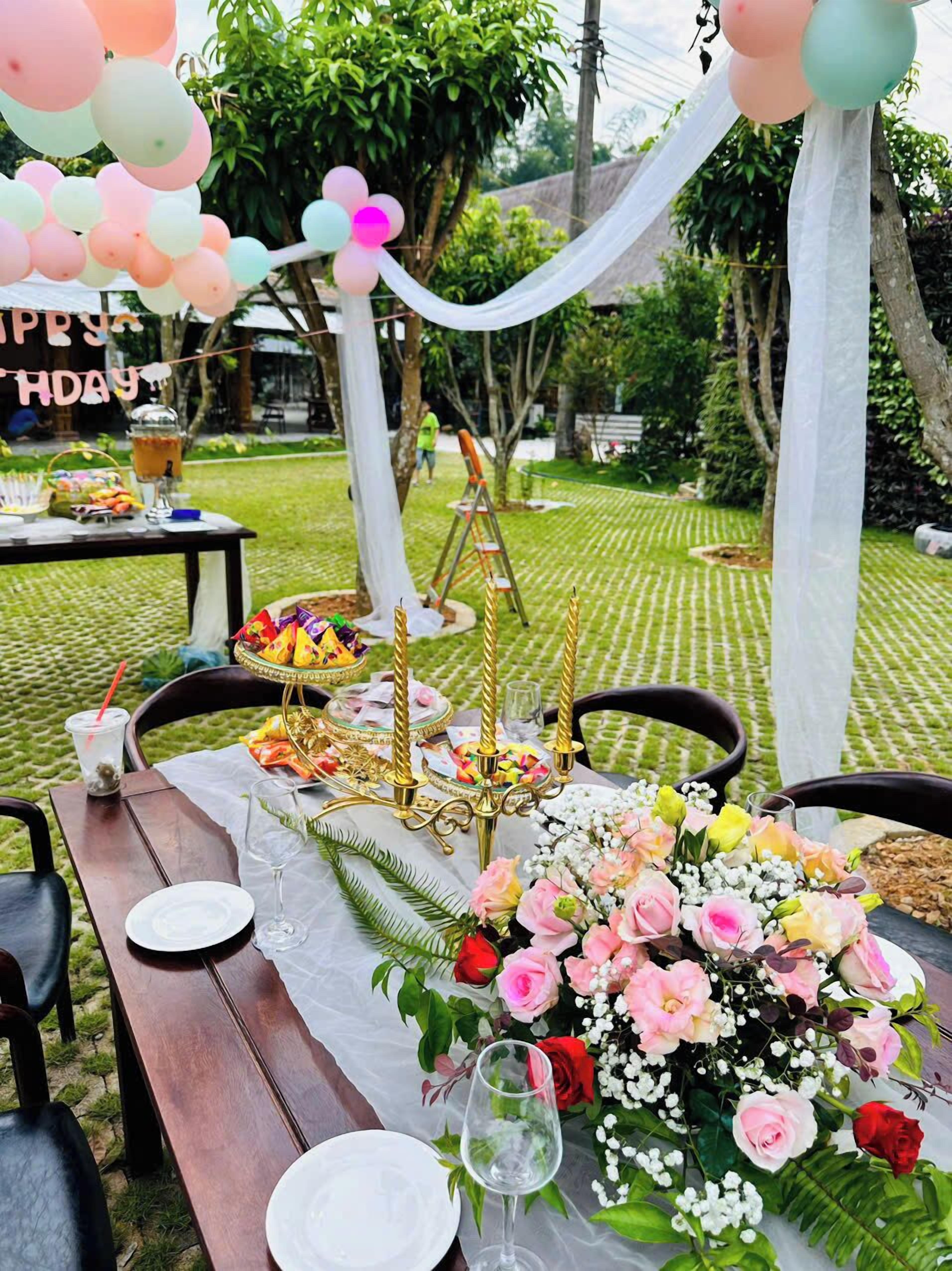 Un área de comedor al aire libre con una mesa dispuesta para una celebración, con un centro de mesa floral, velas y un letrero que dice “5 DE ABRIL”.
