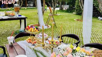 Un área de comedor al aire libre con una mesa dispuesta para una celebración, con un centro de mesa floral, velas y un letrero que dice “5 DE ABRIL”.