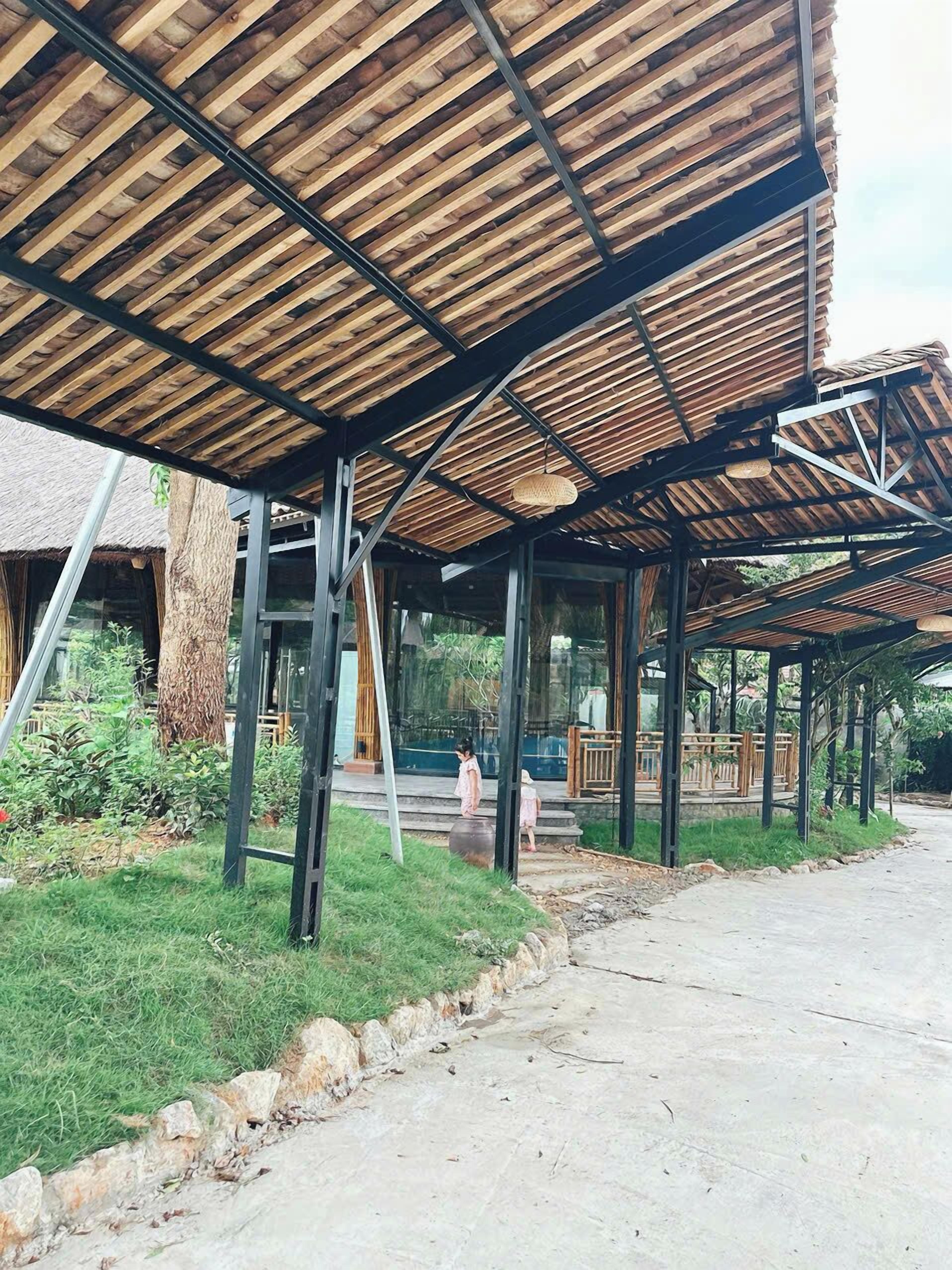 Un espacio al aire libre techado con estructura de madera, cerramiento de vidrio y un camino de hormigón.