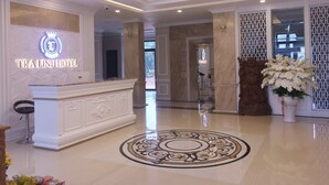 Un vestíbulo de hotel con un mostrador de recepción, una araña de cristal, un diseño decorativo en el suelo y una estatua.