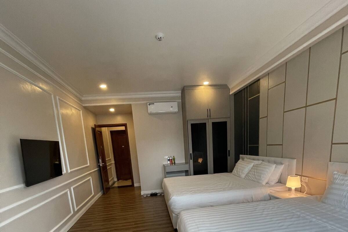 A hotel room with two beds, a TV, a wardrobe, and a bedside table with a lamp.