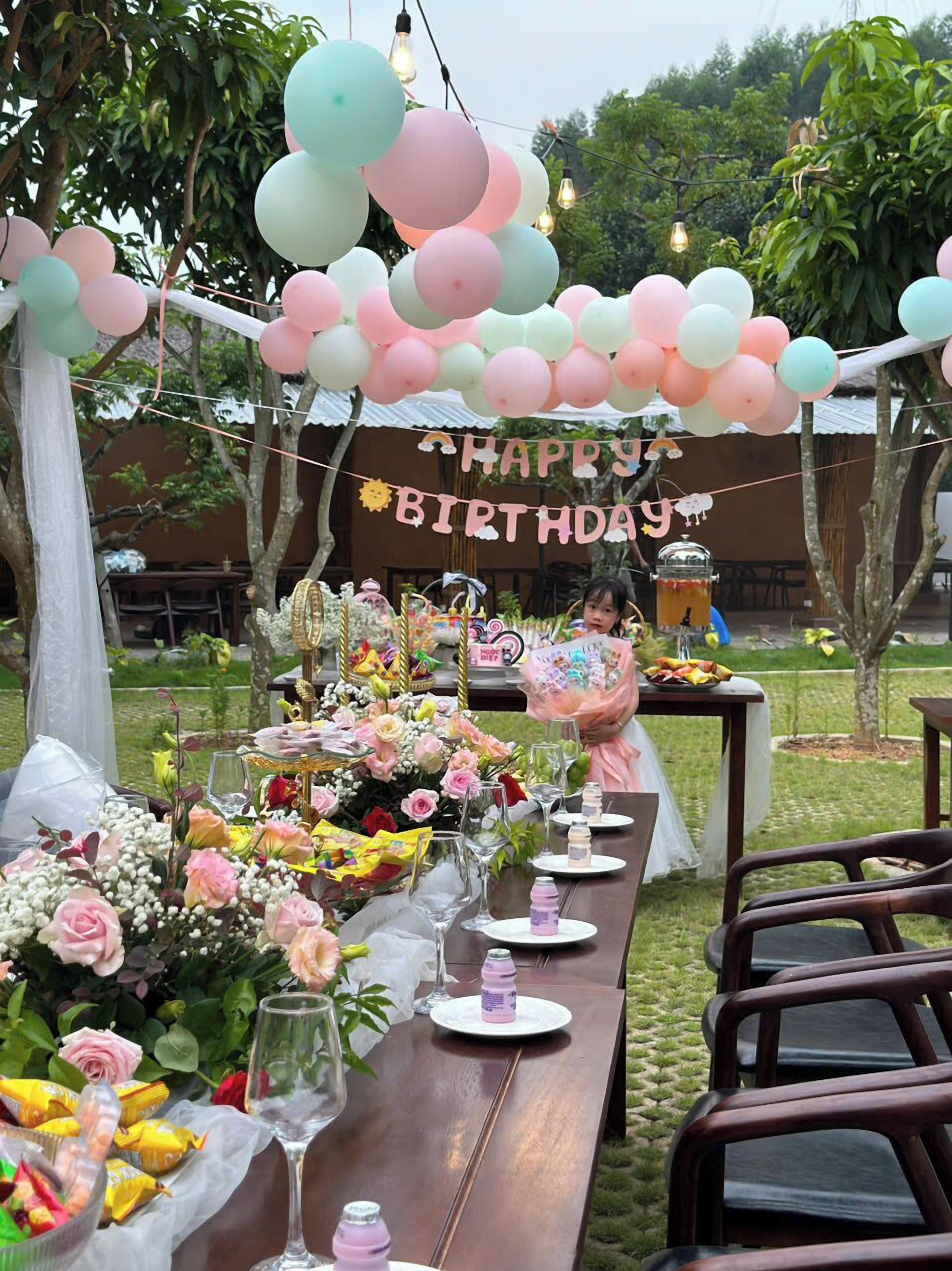 A birthday party setup with a long table decorated with flowers, balloons, and a 'Happy Birthday' banner.