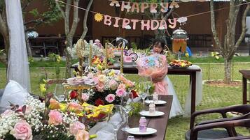 A birthday party setup with a long table decorated with flowers, balloons, and a 'Happy Birthday' banner.