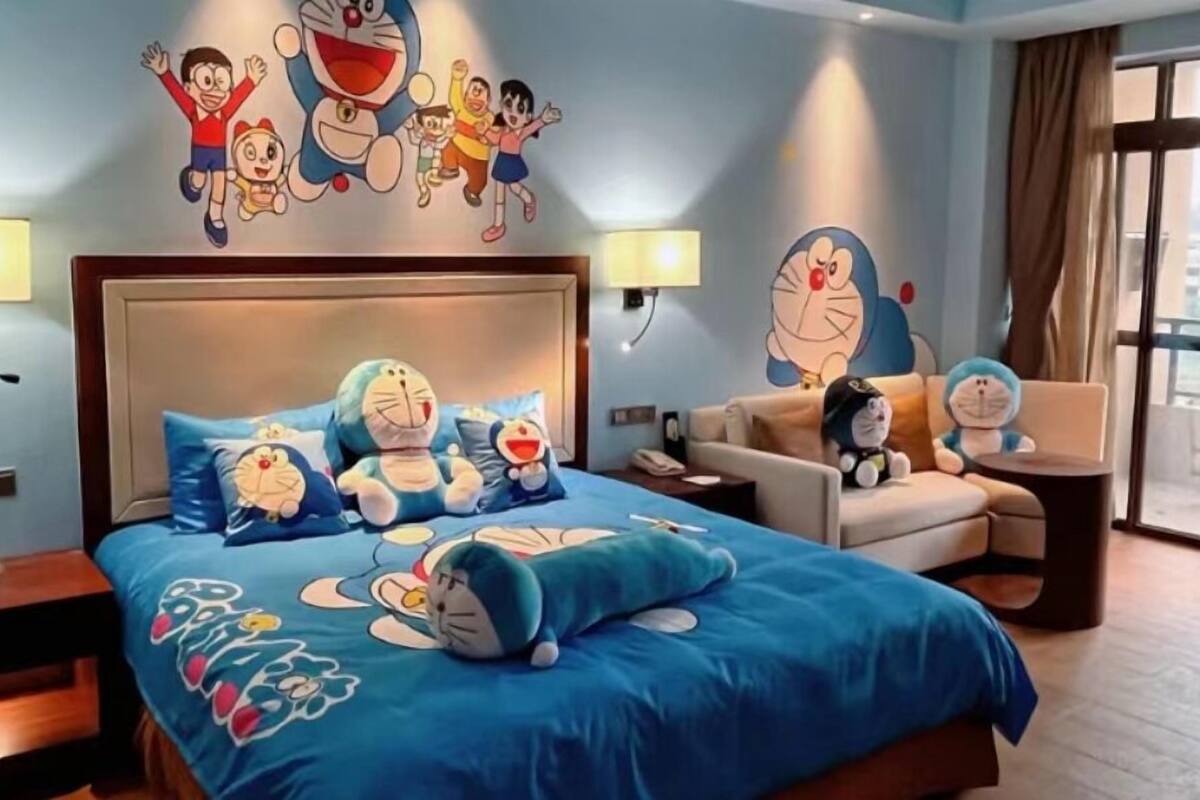 A hotel room with a large bed featuring a blue bedspread with cartoon characters, a sofa, and a small table.