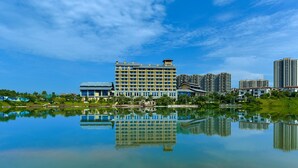 A hotel with a reflection in a calm lake, surrounded by greenery and other buildings. - biguiyuan (Jiangmen)