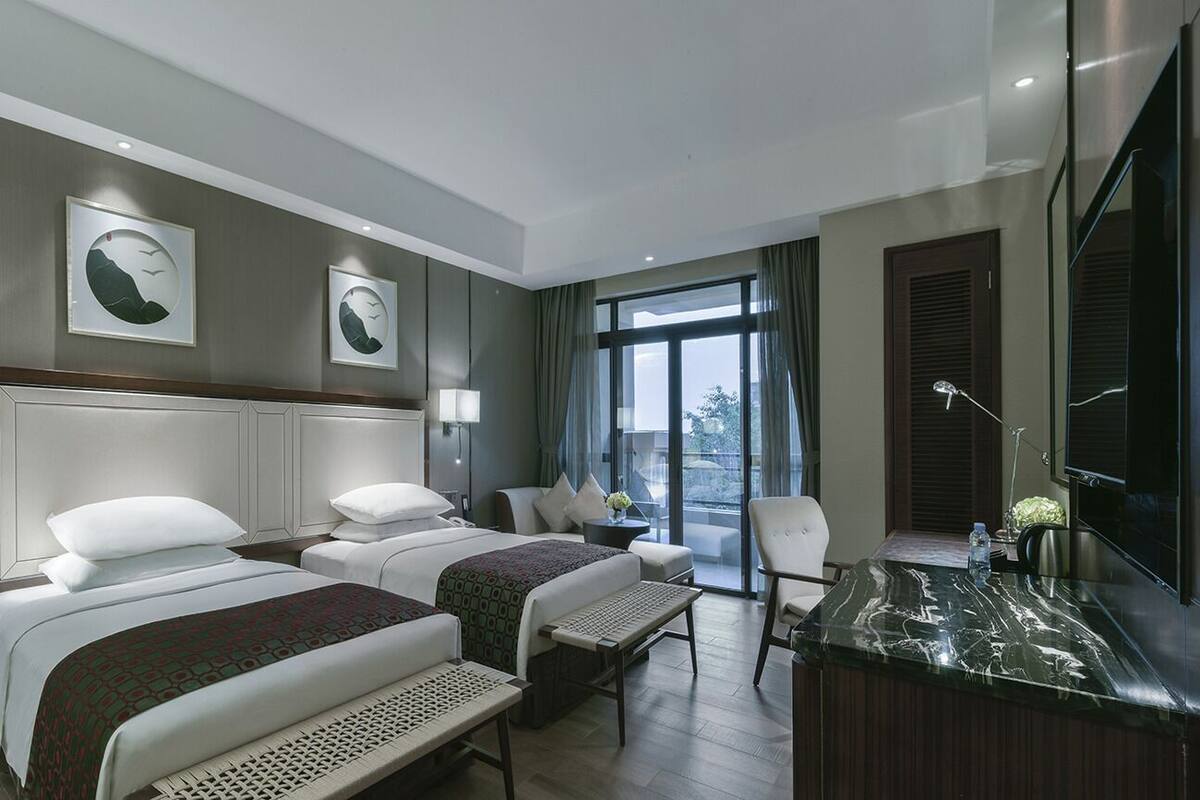 A hotel room with two beds, a desk, a chair, and a large window.