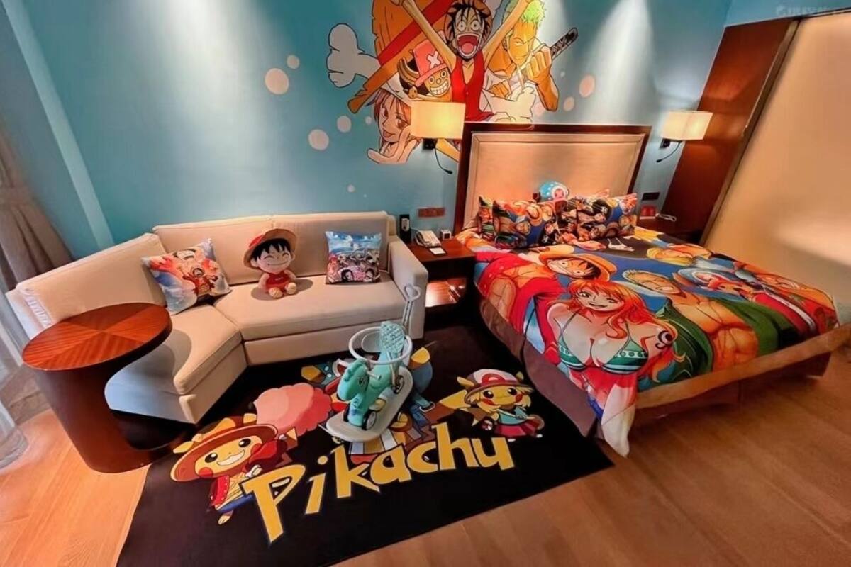 A hotel room decorated with anime characters, including a bed with a colorful blanket and a sofa with pillows.