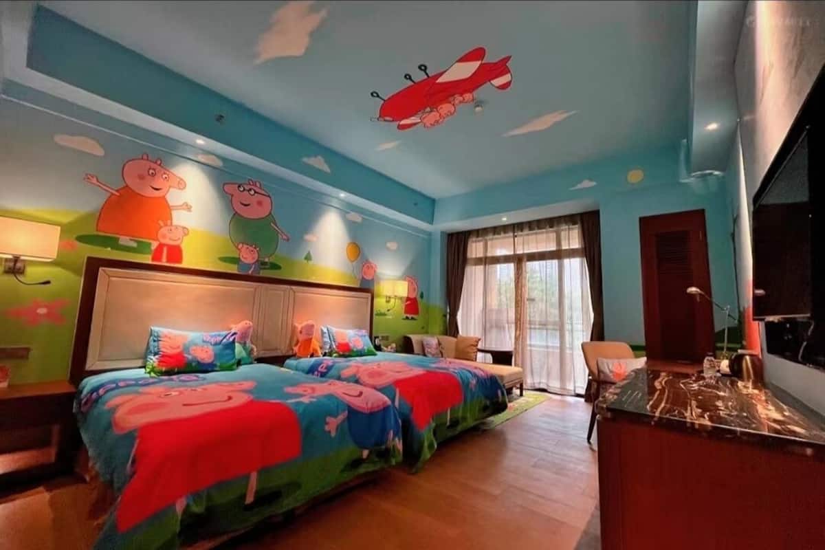 A children's room with two beds, colorful wall murals, and a red airplane on the ceiling.