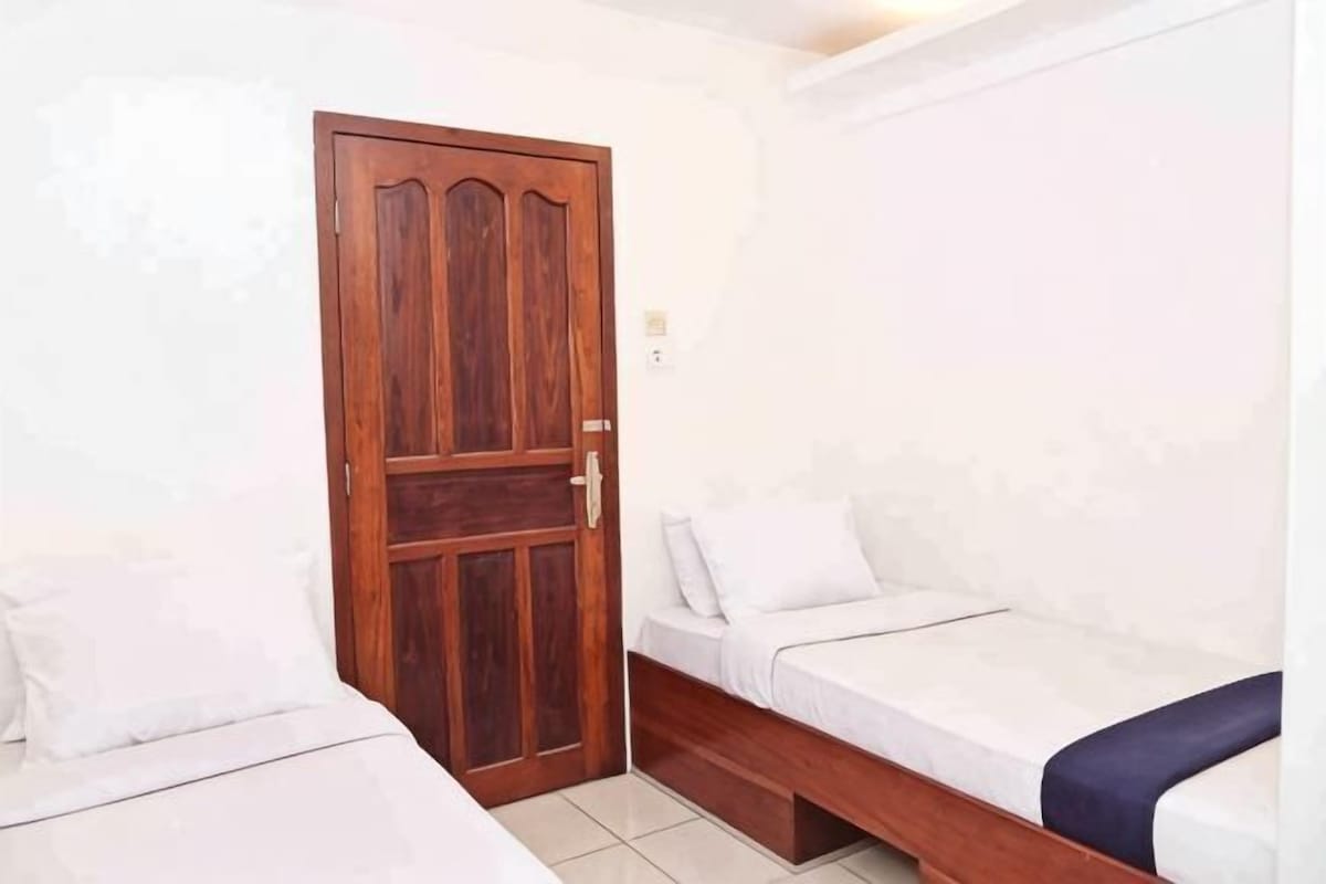 A room with a wooden door, two single beds, and a small bench.