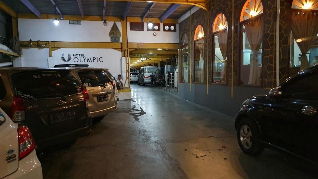 A parking area with several cars, a white van, and a building with a sign reading "Hotel Olympic".