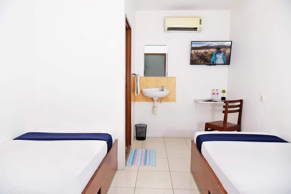 Een hotelkamer met twee bedden, een wastafel, een spiegel, een televisie en een klein bureau met een stoel.