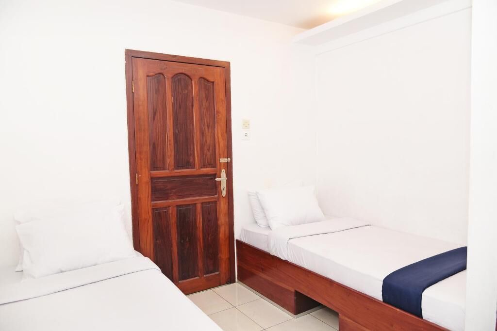A small, clean room with two single beds, a wooden door, and white walls.