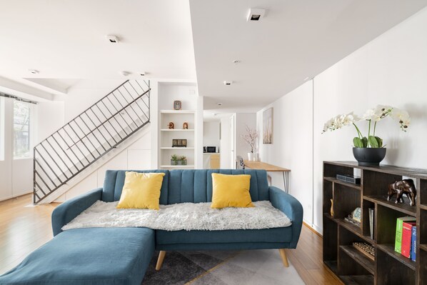 Relax in this inviting living room with a cozy sofa, bookshelf, and potted plant.