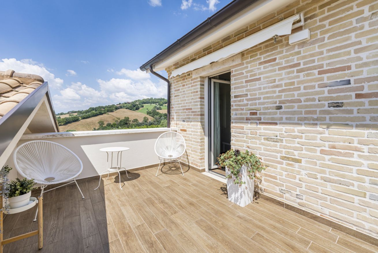 A rooftop terrace with a brick wall, a sliding glass door, and a seating area with two chairs and a table.