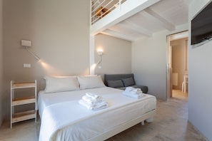 A bedroom with a large bed, a bedside table, a wall-mounted TV, and a staircase leading to an upper level.