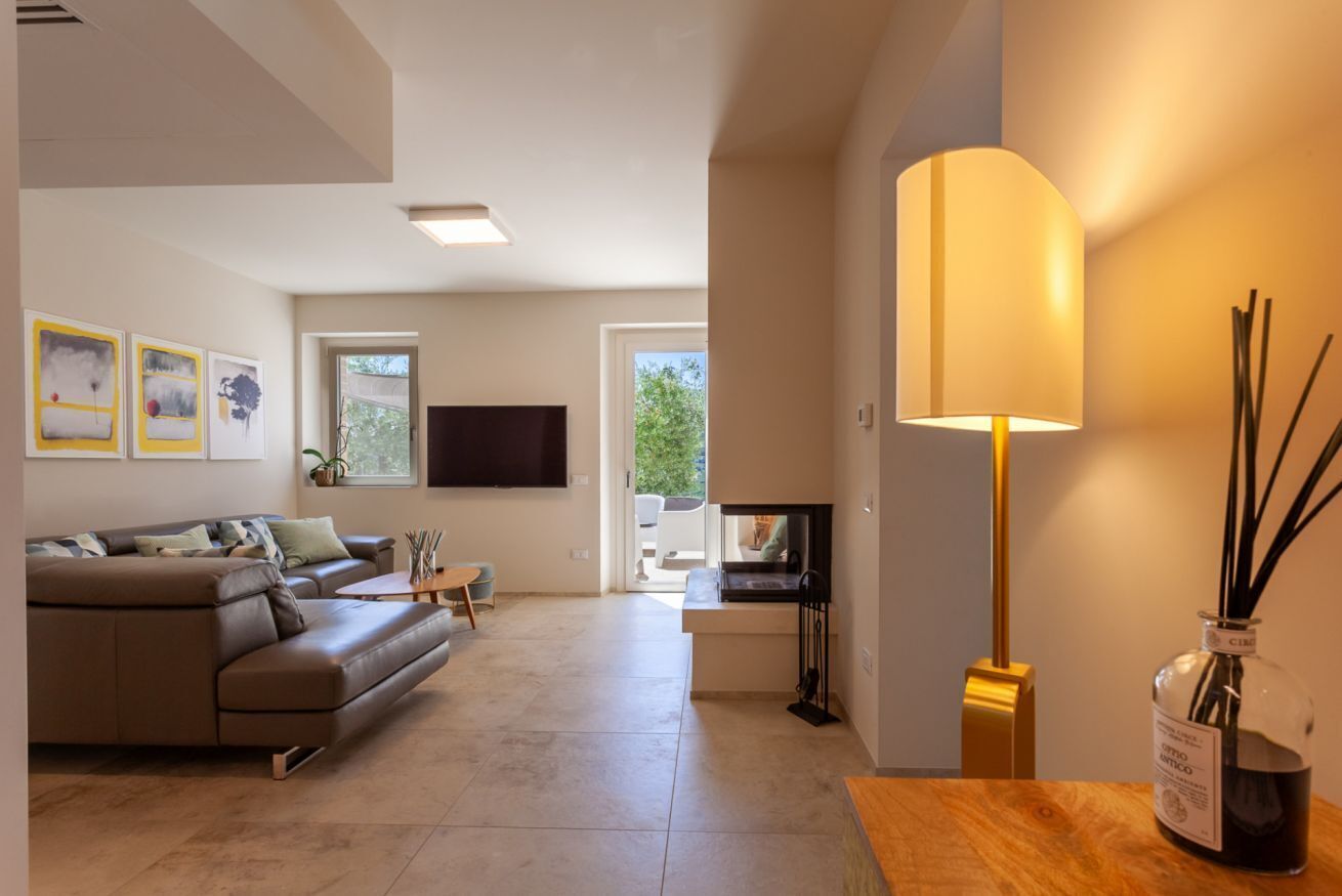 A modern living room with a sofa, coffee table, and a flat-screen TV. There is a window with a view of greenery outside.