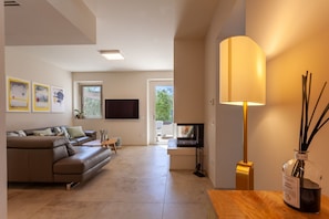 A modern living room with a sofa, coffee table, and a flat-screen TV. There is a window with a view of greenery outside.