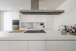 A modern kitchen with white cabinetry, a stainless steel oven, a large island with a sink, and a coffee machine. - Villa Ada by MMega Villas  (Lapedona)