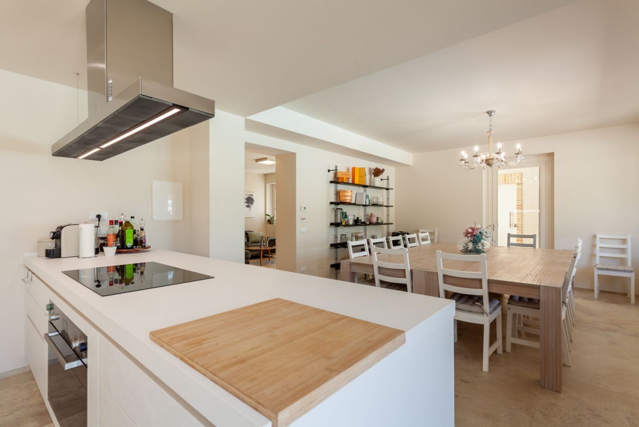A modern kitchen with a central island, a dining area with a wooden table and chairs, and a built-in bookshelf.