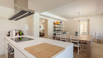 A modern kitchen with a central island, a dining area with a wooden table and chairs, and a built-in bookshelf.
