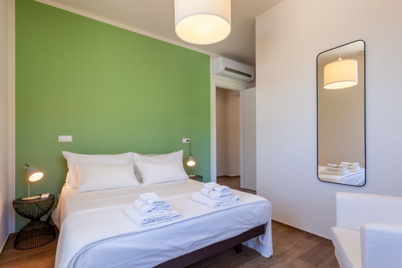 A hotel room with a bed, bedside lamps, a mirror, and a wall-mounted air conditioning unit.