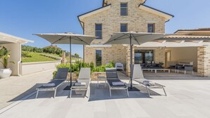 A modern house with a patio area featuring multiple lounge chairs and umbrellas. - Villa Ada by MMega Villas  (Lapedona)