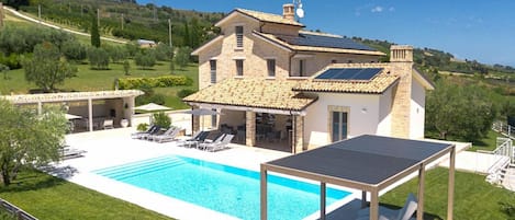A villa with a swimming pool, outdoor seating, and a solar panel.