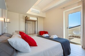 A modern hotel room with a large bed, a red chair, a balcony with a view, and a ceiling fan.