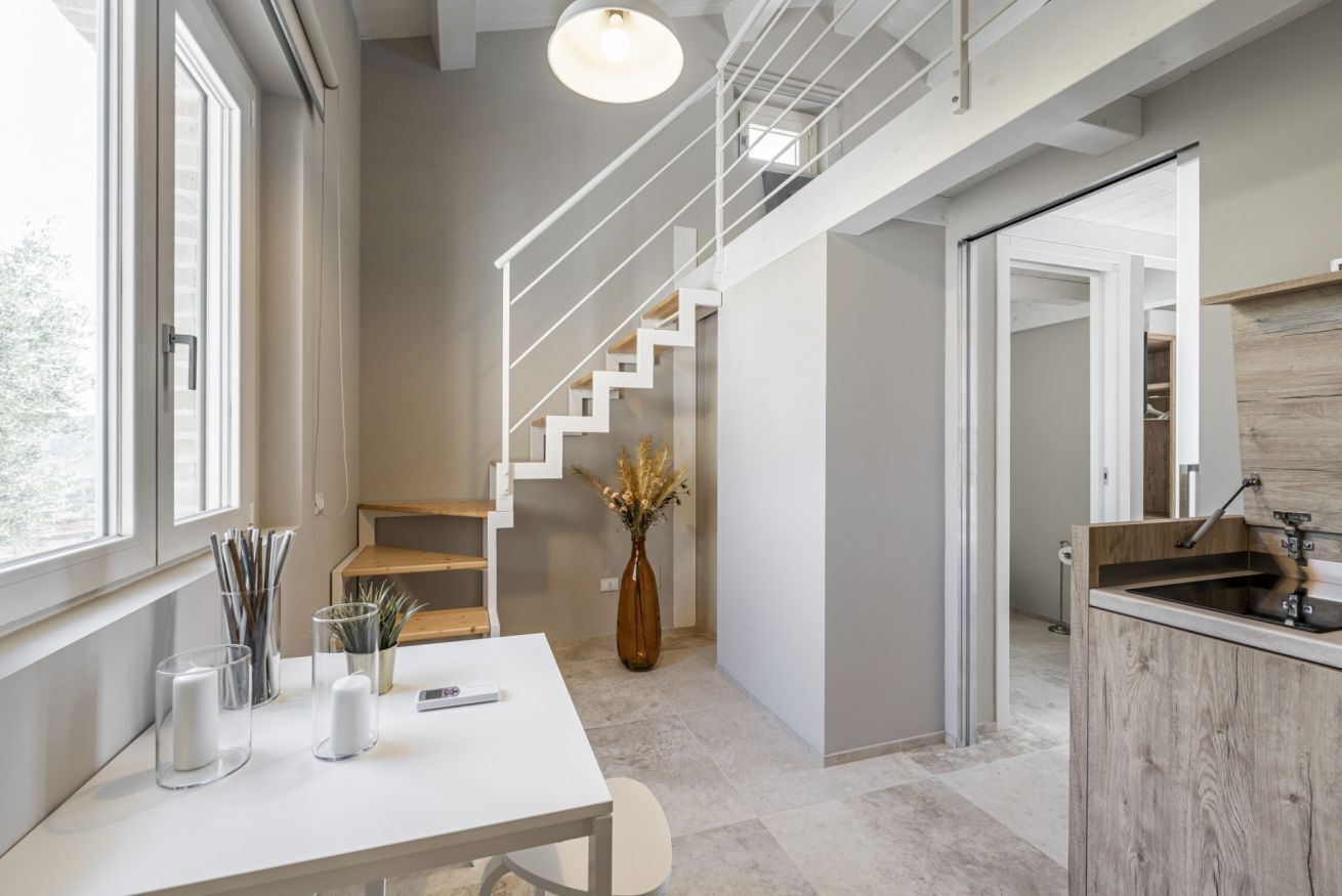 A modern interior with a staircase, a dining area with a table and chairs, and a kitchen area.