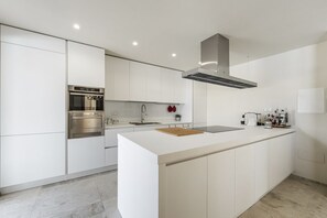 A modern kitchen with white cabinetry, a stainless steel oven, and a large island with a cutting board.