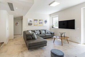 A modern living room with a sectional sofa, a round coffee table, and a flat-screen TV mounted on the wall.