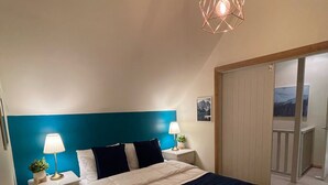 A bedroom with a bed, bedside tables, a lamp, a hanging light fixture, and a view of a balcony. - Maddison-Chalet (Dinner Plain)