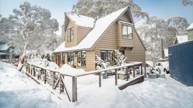 A two-story house with a sloped roof, surrounded by snow-covered trees and a wooden fence. - Maddison-Chalet (Dinner Plain)