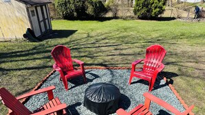 Un espace patio comprenant quatre chaises Adirondack rouges et une table ronde noire, le tout entouré de gravier.