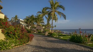 Un sendero empedrado que lleva a una playa con palmeras y una construcción de techo de paja.
