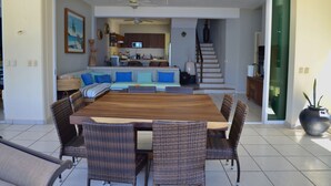 Un comedor con una mesa de madera y sillas de mimbre, una cocina al fondo y una escalera que sube a un nivel superior.