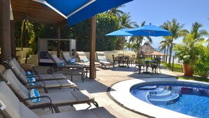 Zona junto a la piscina con sillones de descanso, sombrillas y una pileta.