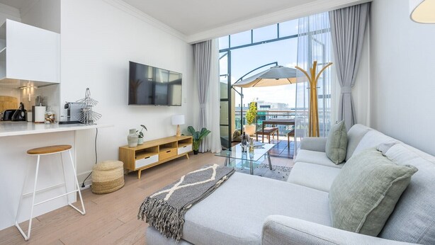 A modern living room with a sofa, TV, and dining area with a balcony. - Carefree living in the heritage (Auckland)