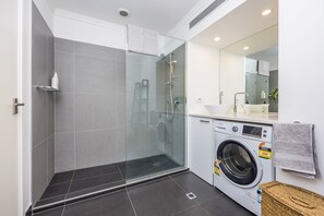 A modern bathroom with a glass-enclosed shower, a built-in washing machine, and a large mirror.