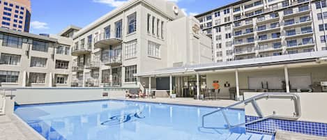 A swimming pool with a view of a modern building with balconies and a tower.
