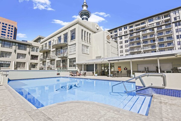A swimming pool with a view of a modern building with balconies and a tower.