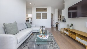 A modern living room with a glass coffee table, a white sofa, and a TV mounted on the wall. - Carefree living in the heritage (Auckland)