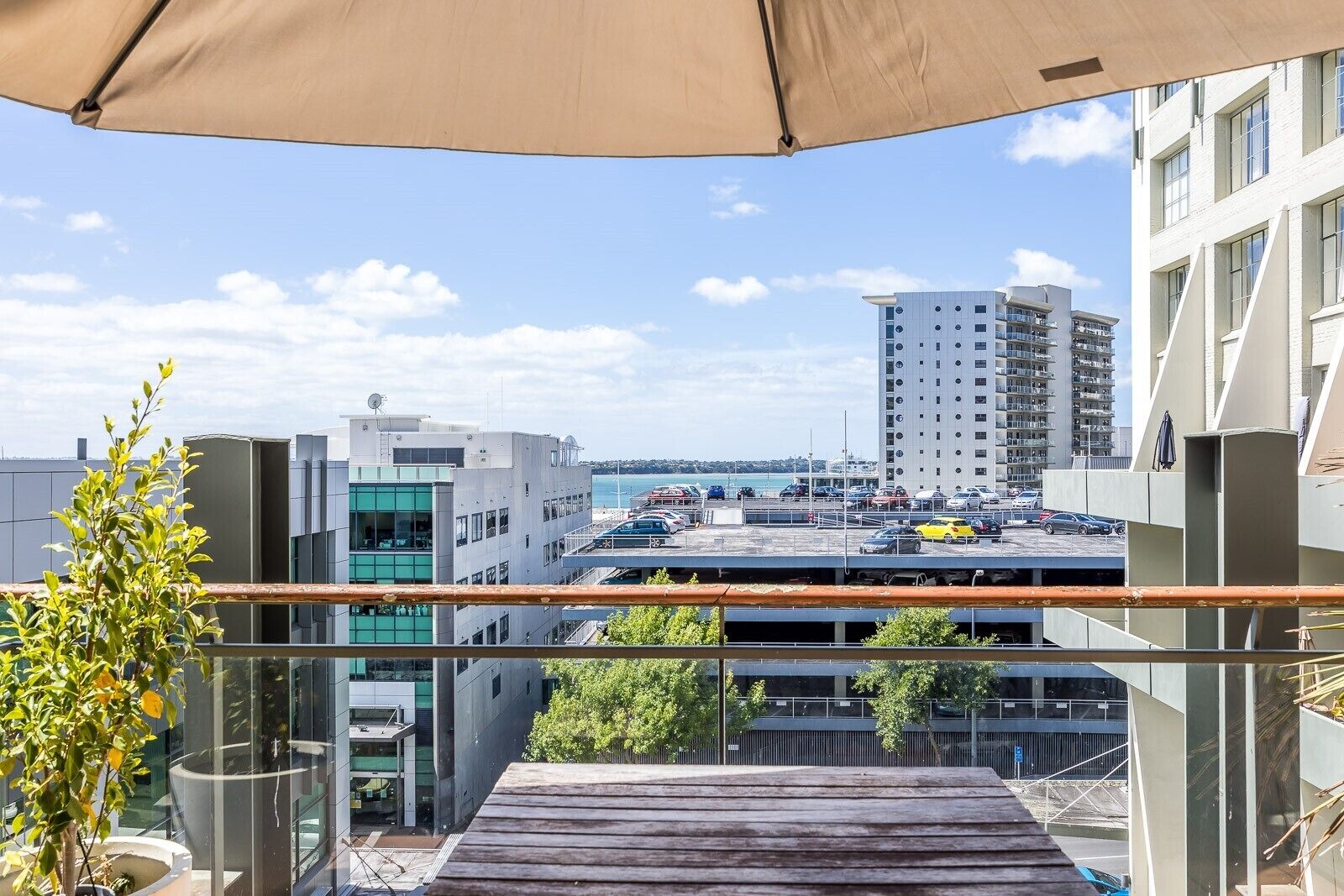Un balcon donnant sur un parking et sur des immeubles, notamment un grand bâtiment blanc et une structure moderne aux fenêtres en verre.