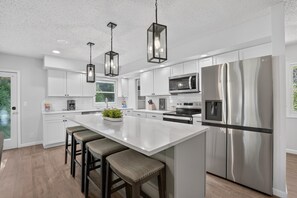 Une cuisine moderne avec des meubles blancs, des appareils en acier inoxydable et un îlot central doté de tabourets de bar.