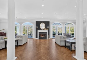 A spacious room with a fireplace, two sofas, a piano, and large windows.