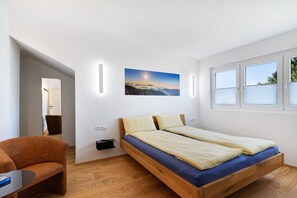 Una habitación con una cama de madera, una silla, una mesita y un cuadro en la pared.