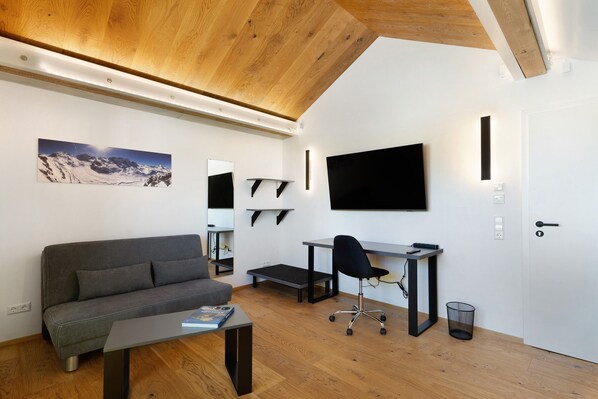 A modern room with a wooden ceiling, a gray sofa, a desk with a chair, a mounted TV, and a bookshelf. - Holiday Apartment "Wolf's Ortenau" with Balcony & Wi-Fi (Renchen)