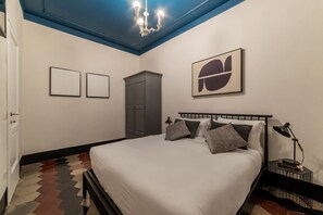 Un dormitorio con cama, lámpara de araña, armario y dos cuadros en la pared.